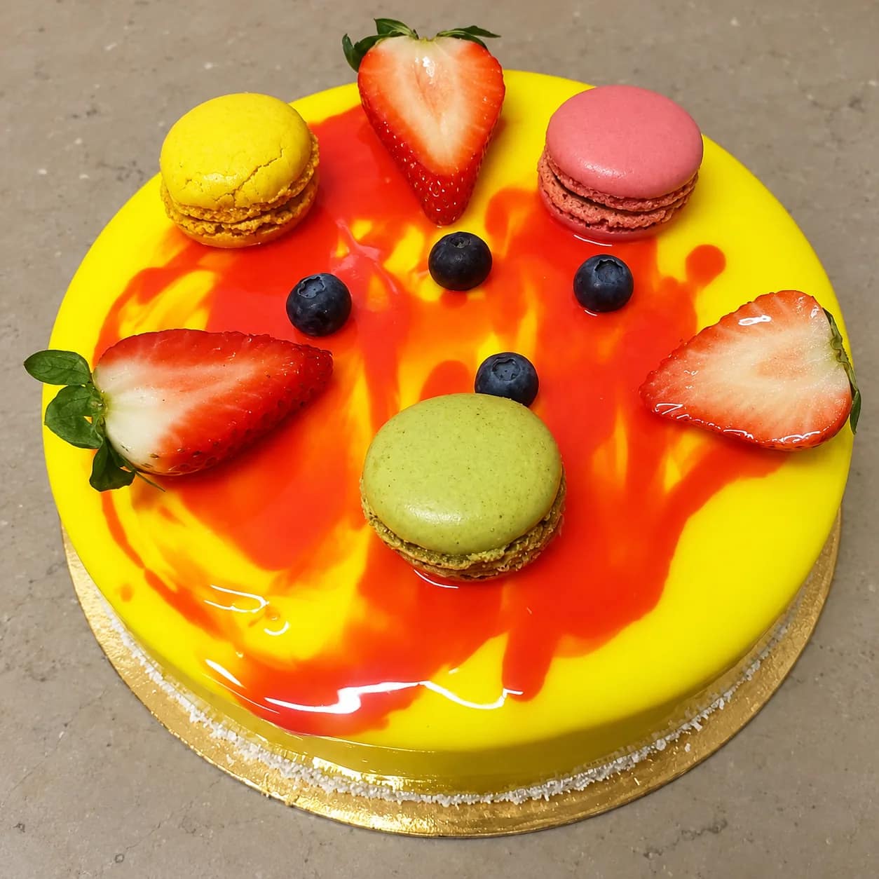 Entremets au glaçage miroir jaune et rouge, décoré de macarons, de fraises et de myrtilles