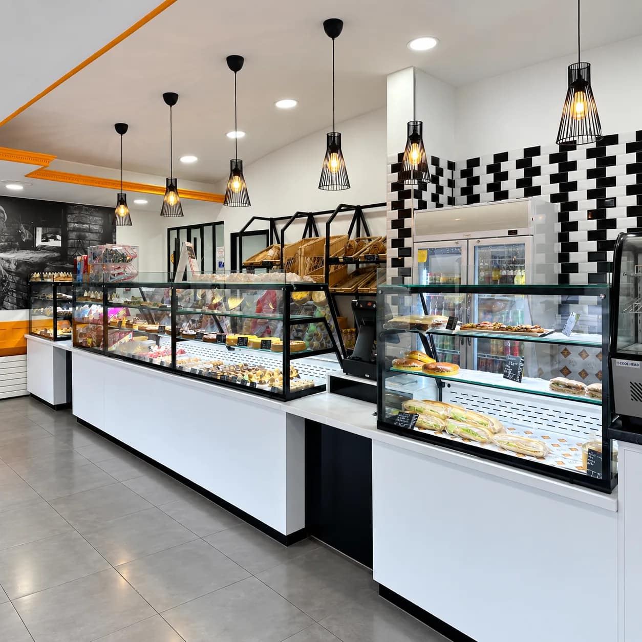 Intérieur de la boutique : comptoirs vitrés de pâtisseries, sandwichs, pains en corbeilles et boissons fraîches