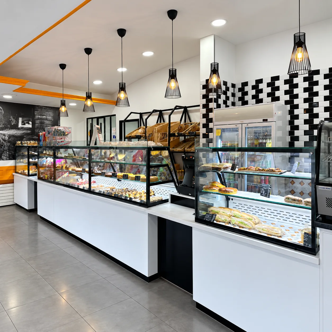Intérieur de la boutique : comptoirs vitrés de pâtisseries, sandwichs, pains en corbeilles et boissons fraîches
