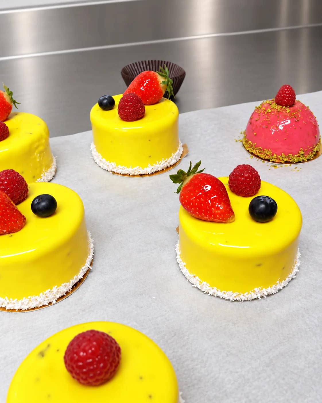 Entremets individuels au glaçage jaune, surmontés de fraises, framboises et myrtilles