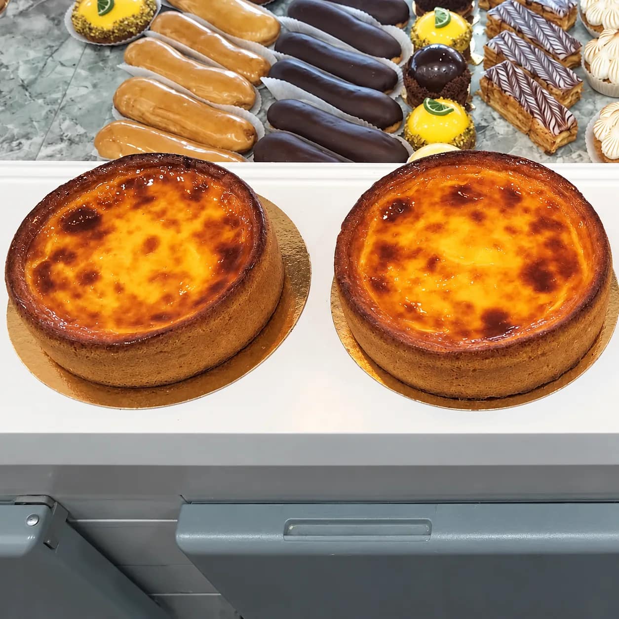 Deux flans pâtissiers à la surface caramélisée, devant une rangée d’éclairs et de mille-feuilles